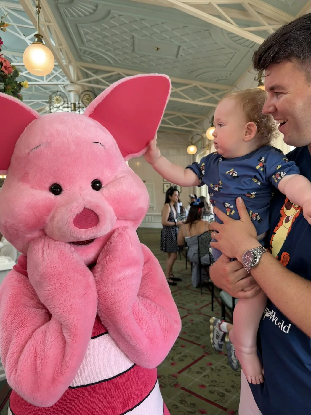 George reaching towards Piglet’s ear while Adam holds him in the restaurant