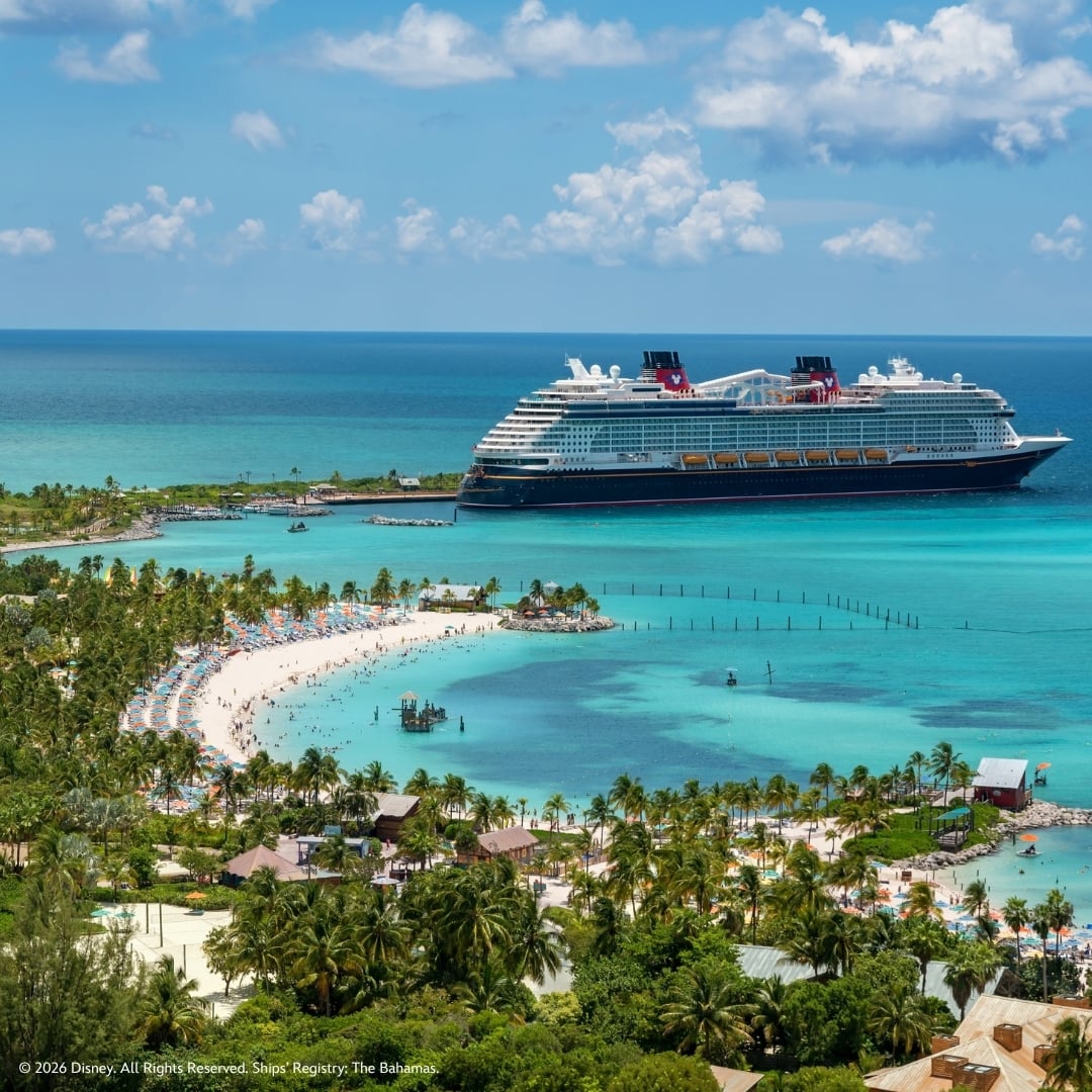 Disney Wish docked at Disney Castaway Cay beside turquoise water and a palm-lined beach