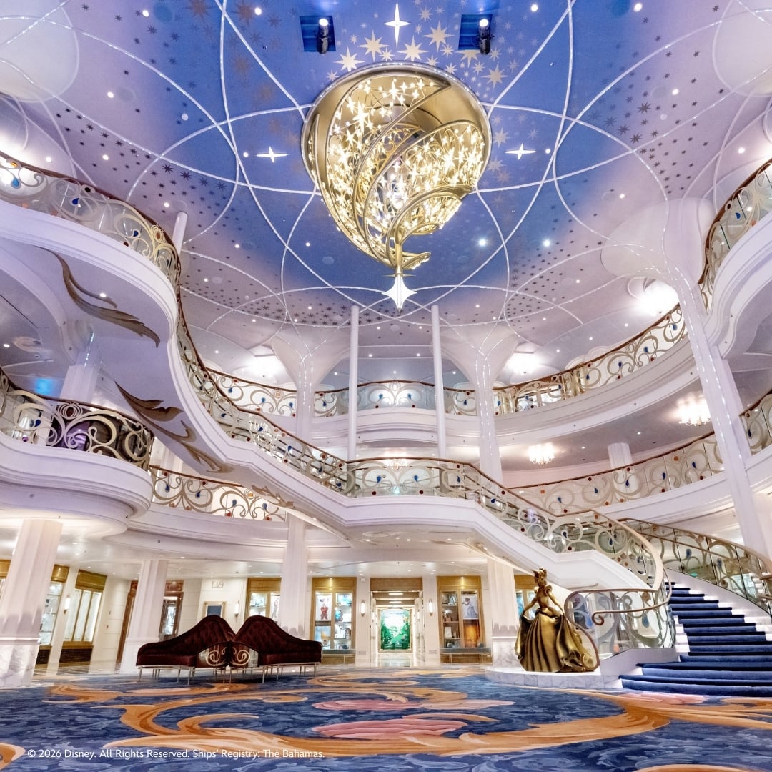 The Grand Hall aboard Disney Wish, with its sweeping staircase and illuminated chandelier
