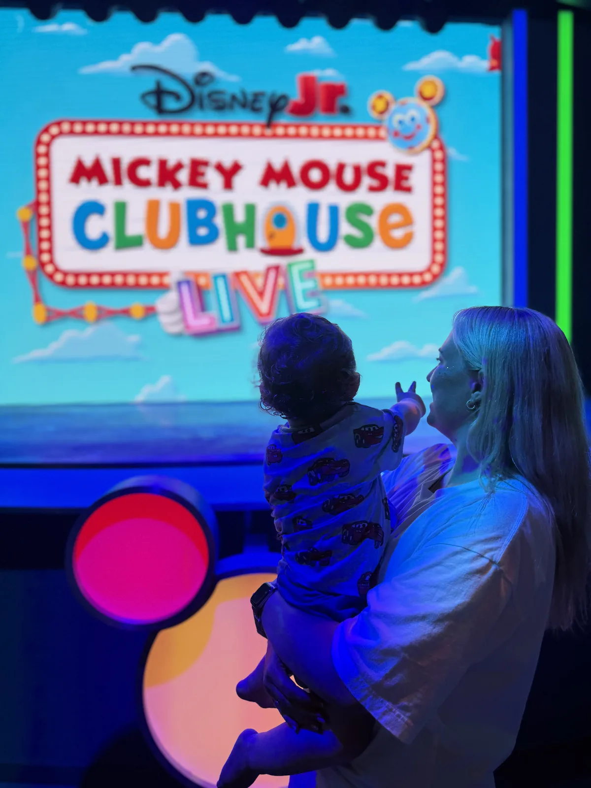 Jodie holding George in front of the Disney Jr. Mickey Mouse Clubhouse Live! screen