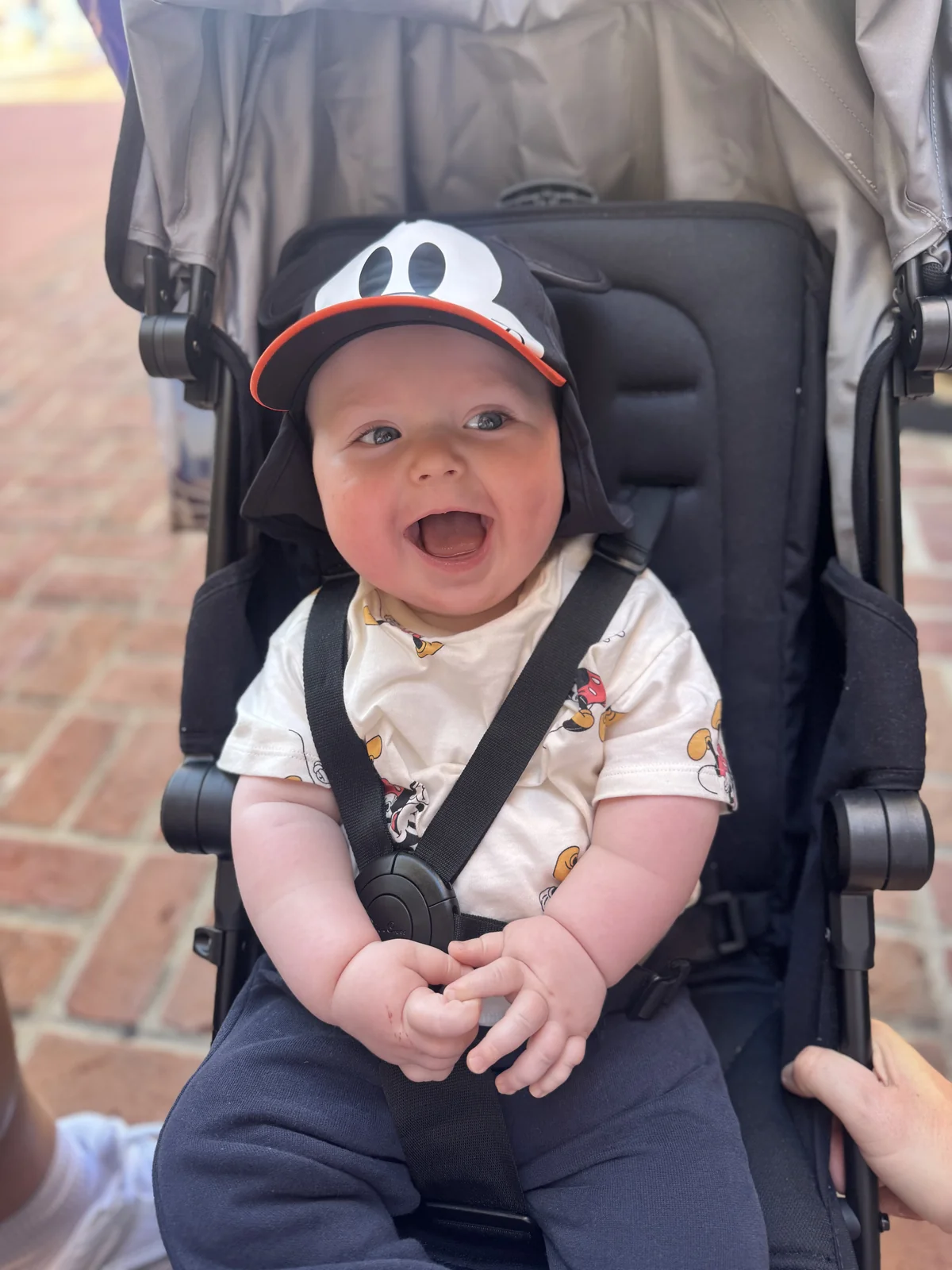 George smiling in his pushchair, wearing his Mickey Mouse cap