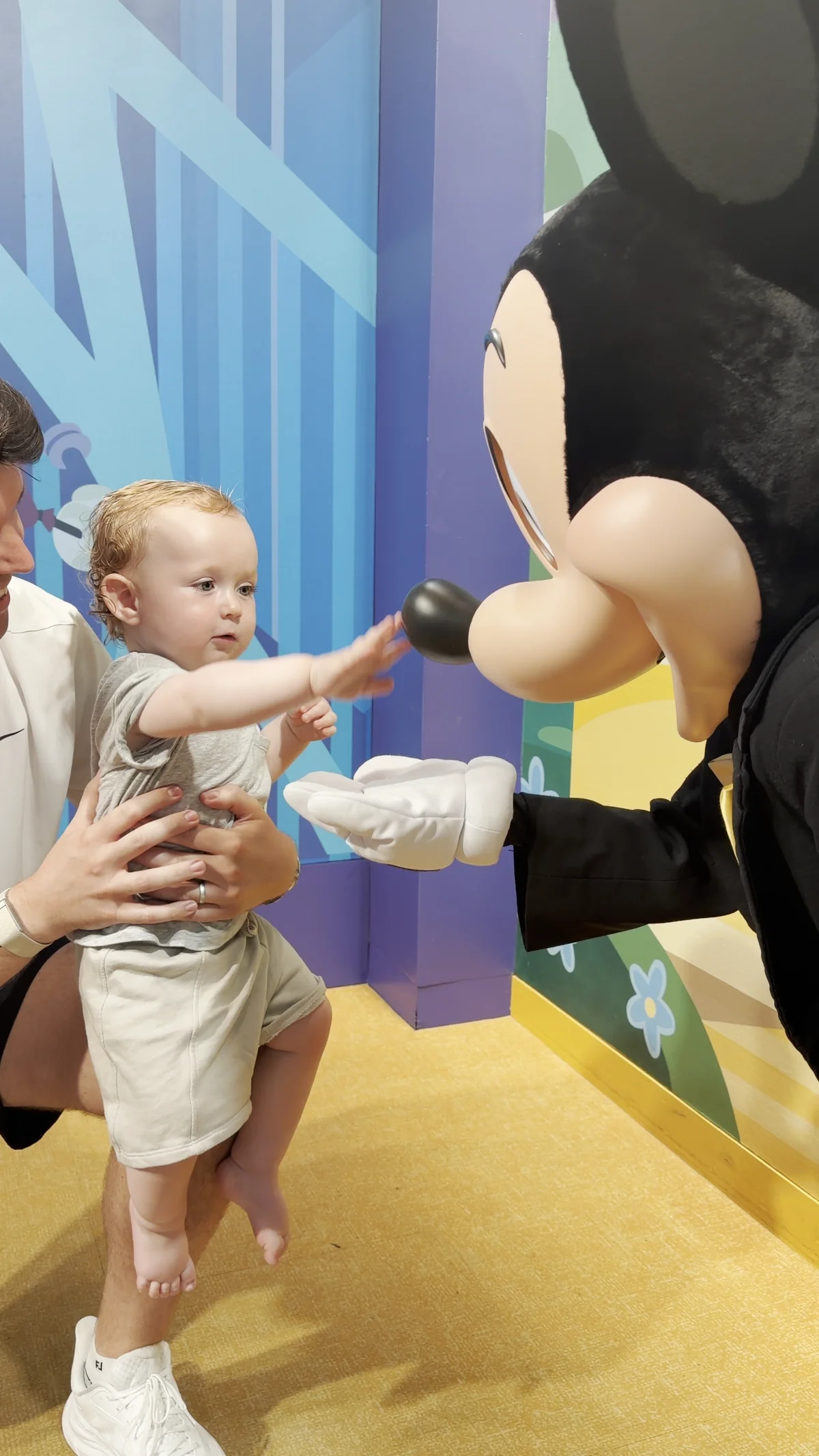 George reaching towards Mickey Mouse’s nose while Adam holds him