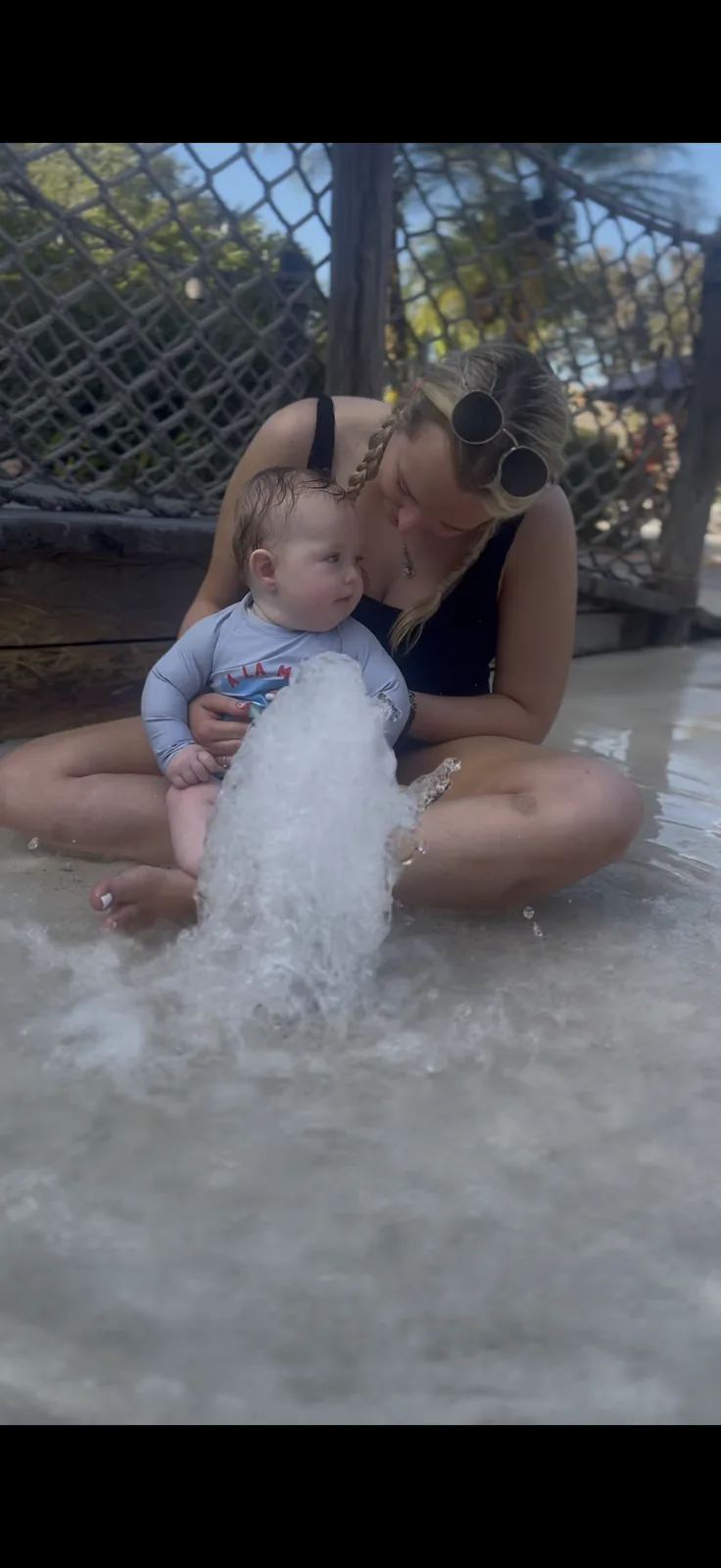 Jodie holding George beside a water jet in the shallow play area at Typhoon Lagoon