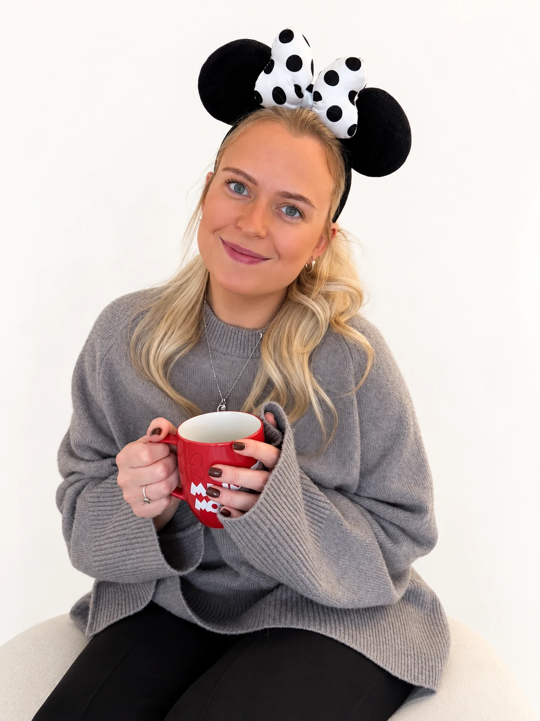 Jodie wearing Minnie ears and holding a red mug against a soft white background